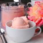 Sugar free cotton candy ice cream in a white bowl with flowers and the ninja creami pint in the background.
