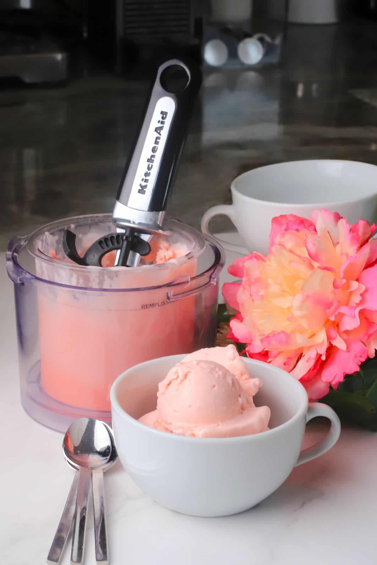 Sugar free cotton candy ice cream in a white bowl with flowers and the ninja creami pint in the background.