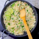 Cilantro Lime Cauliflower Rice in the skillet topped with cilantro and lime slices with a wooden spoon.