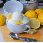 Gelato al limone in a bowl with lemon wedges and lemons around the bowl with spoons resting on a cutting board.