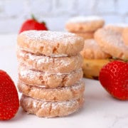 Strawberry sugar free cookies stacked next to more strawberries and cookies.