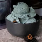 Sugar free licorice ice cream in a black bowl adorned with licorice pieces.
