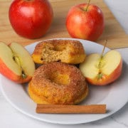 2 low carb apple cinnamon donuts on a plate, one has a bite out of it.