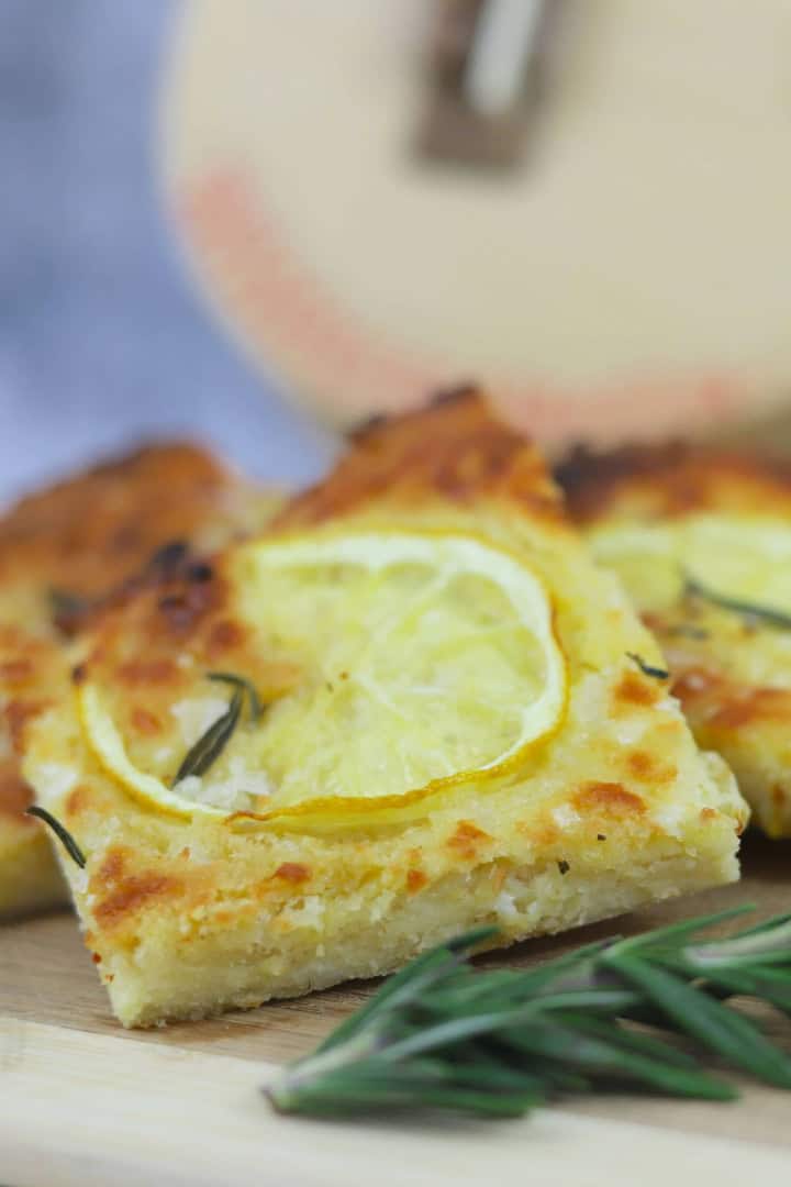 Slices of low carb focaccia on a cutting board with lemon and rosemary, with a guitar in the background.