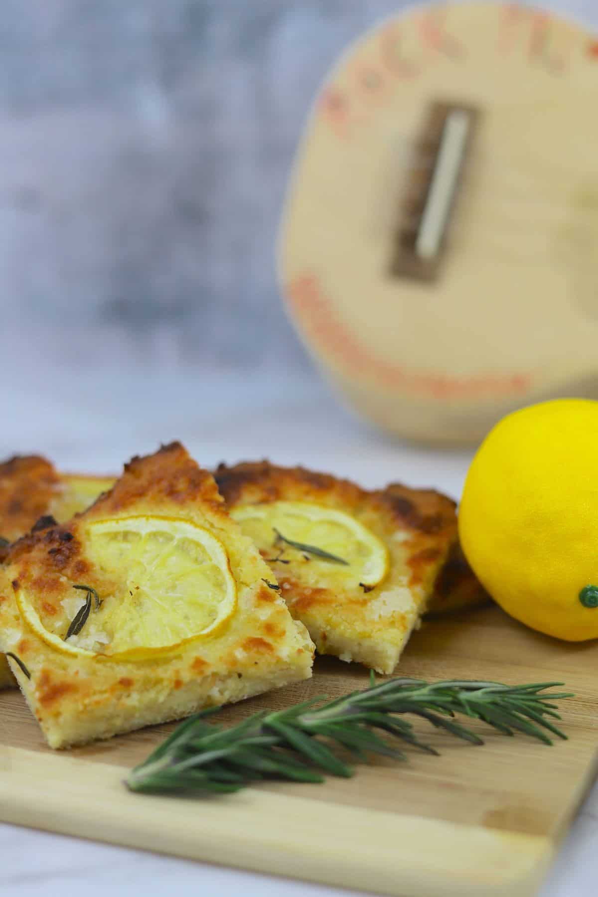 Slices of low carb focaccia on a cutting board with lemon and rosemary, with a guitar in the background.