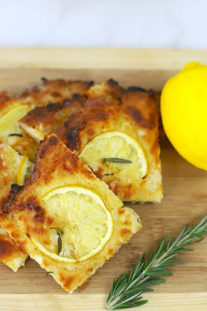 Slices of low carb focaccia on a cutting board with lemon and rosemary.