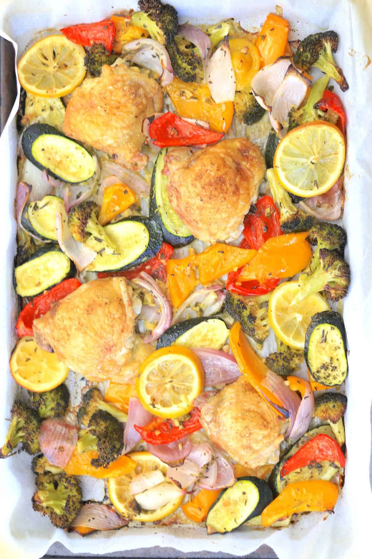 Sheet pan chicken and veggies on a parchment lined baking sheet.