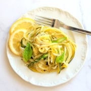 Zucchini veggie pasta on a white plate garnished with lemon slices and fresh basil.