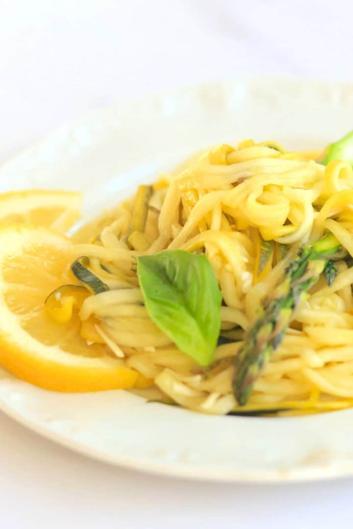 Zucchini veggie pasta on a white plate garnished with lemon slices and fresh basil.