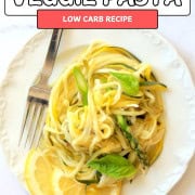 Zucchini veggie pasta on a white plate garnished with lemon slices and fresh basil.