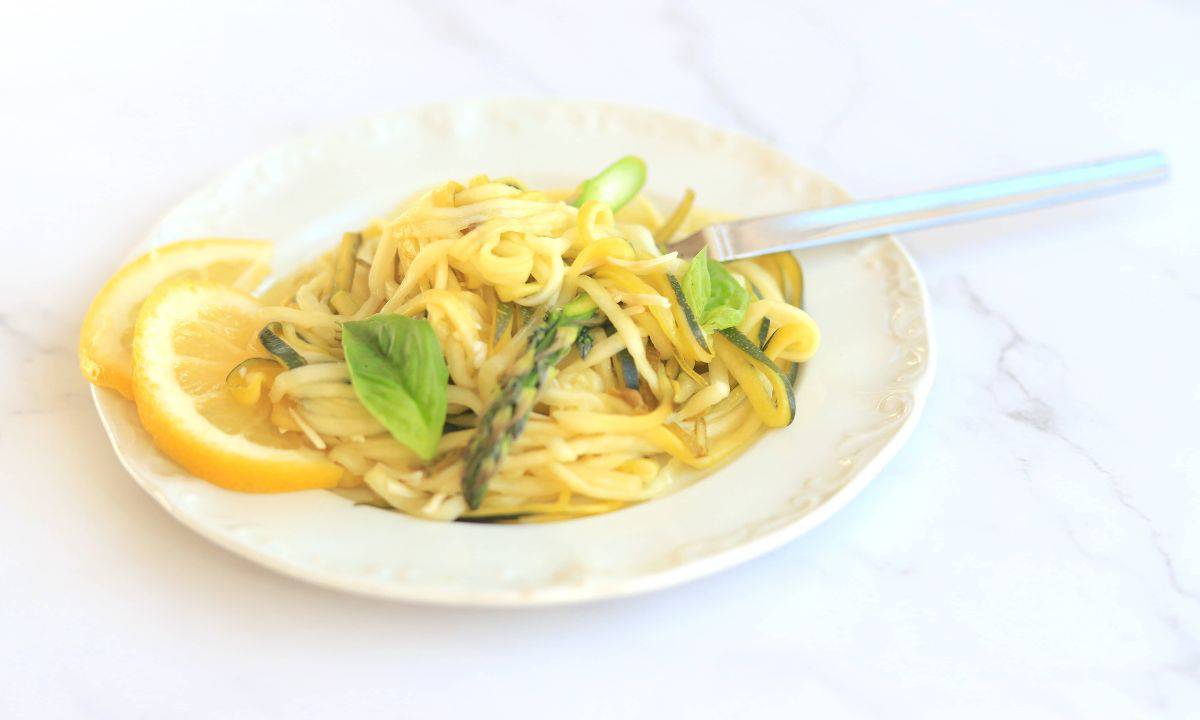 Zucchini veggie pasta on a white plate garnished with lemon slices and fresh basil.
