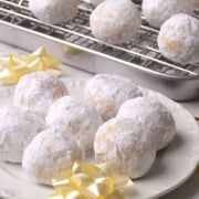 Low carb gluten free snowball cookies on a white plate and more on a wire rack in the background with golden bows.