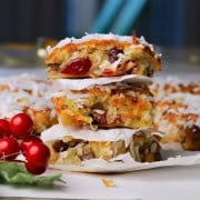 Three low carb cranberry coconut squares stacked on top of each other next to more squares and a cranberry decor.