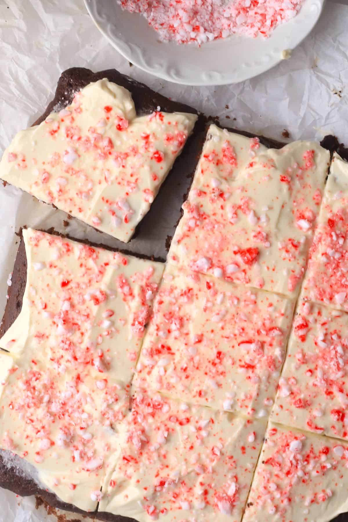 Low carb candy cane chocolate cake squares on a parchment paper with a bowl with crushed peppermint candy.