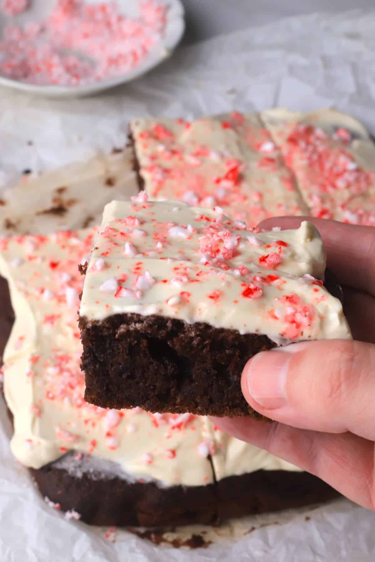 Holding a piece of ow carb candy cane chocolate cake squares in hand with the cake in the background.