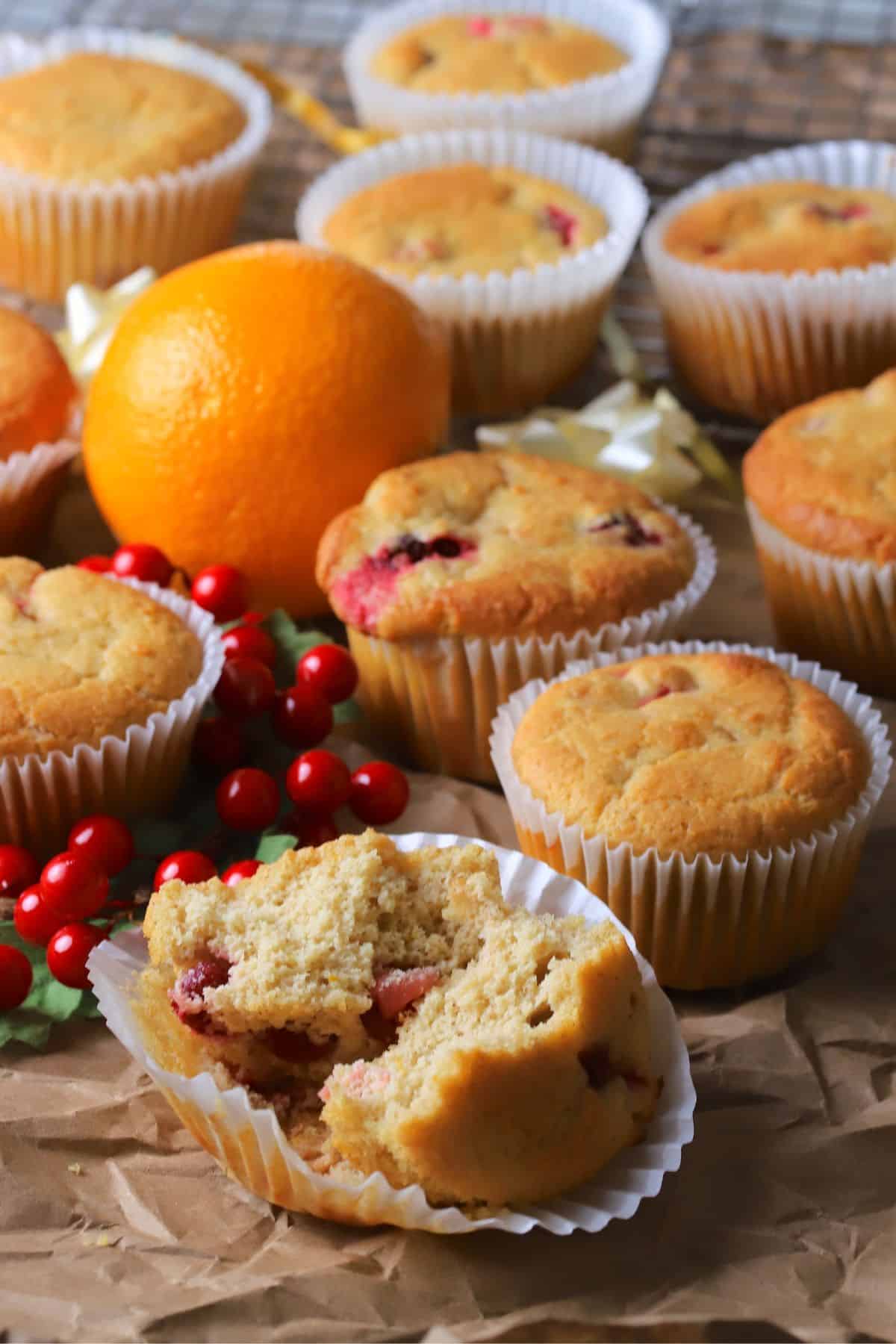Several low carb cranberry orange muffins on a brown paper with cranberries and an orange.
