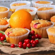 Several low carb cranberry orange muffins on a brown paper with cranberries and an orange.
