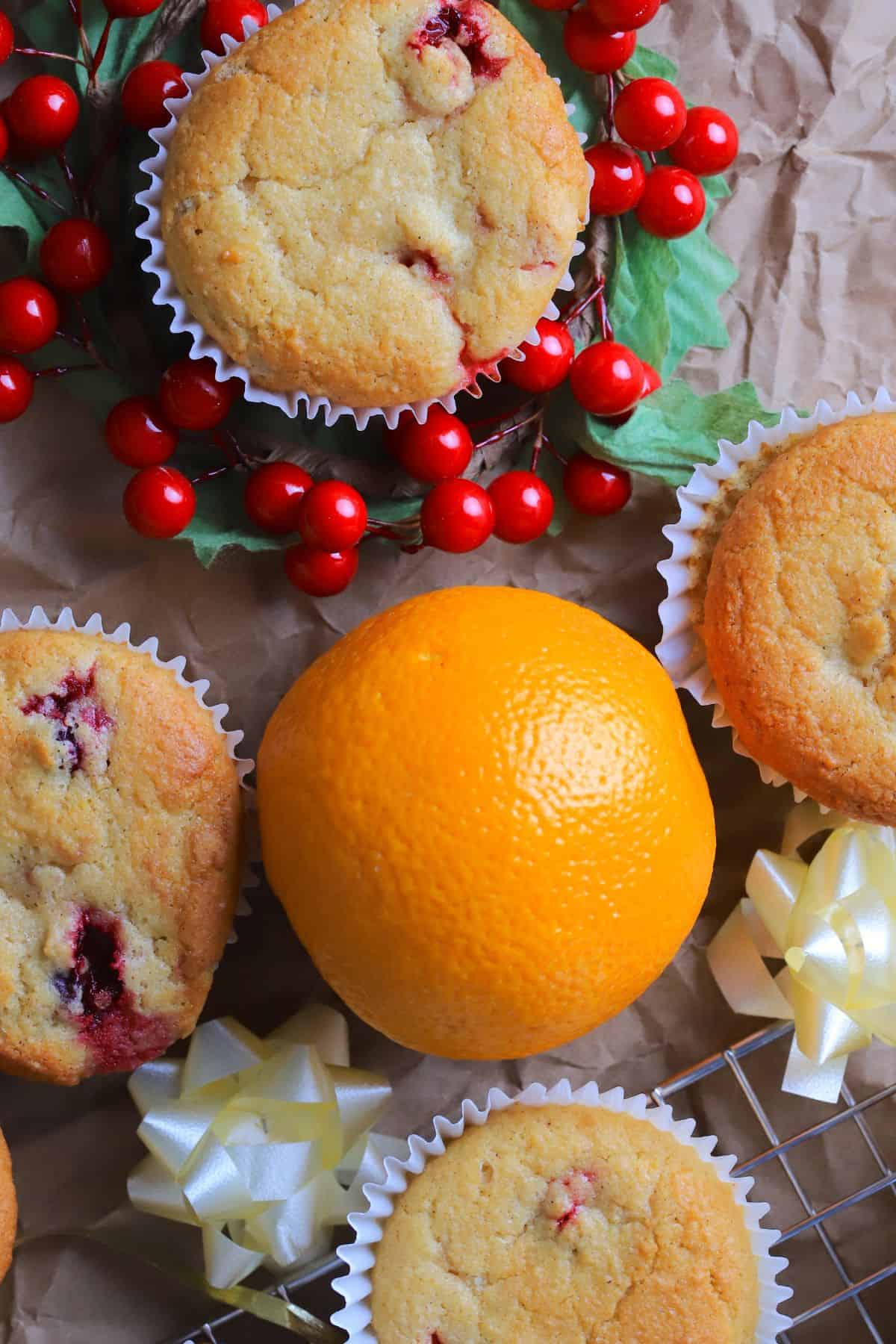 Overhead shot of Several low carb cranberry orange muffins on a brown paper with cranberries and an orange.