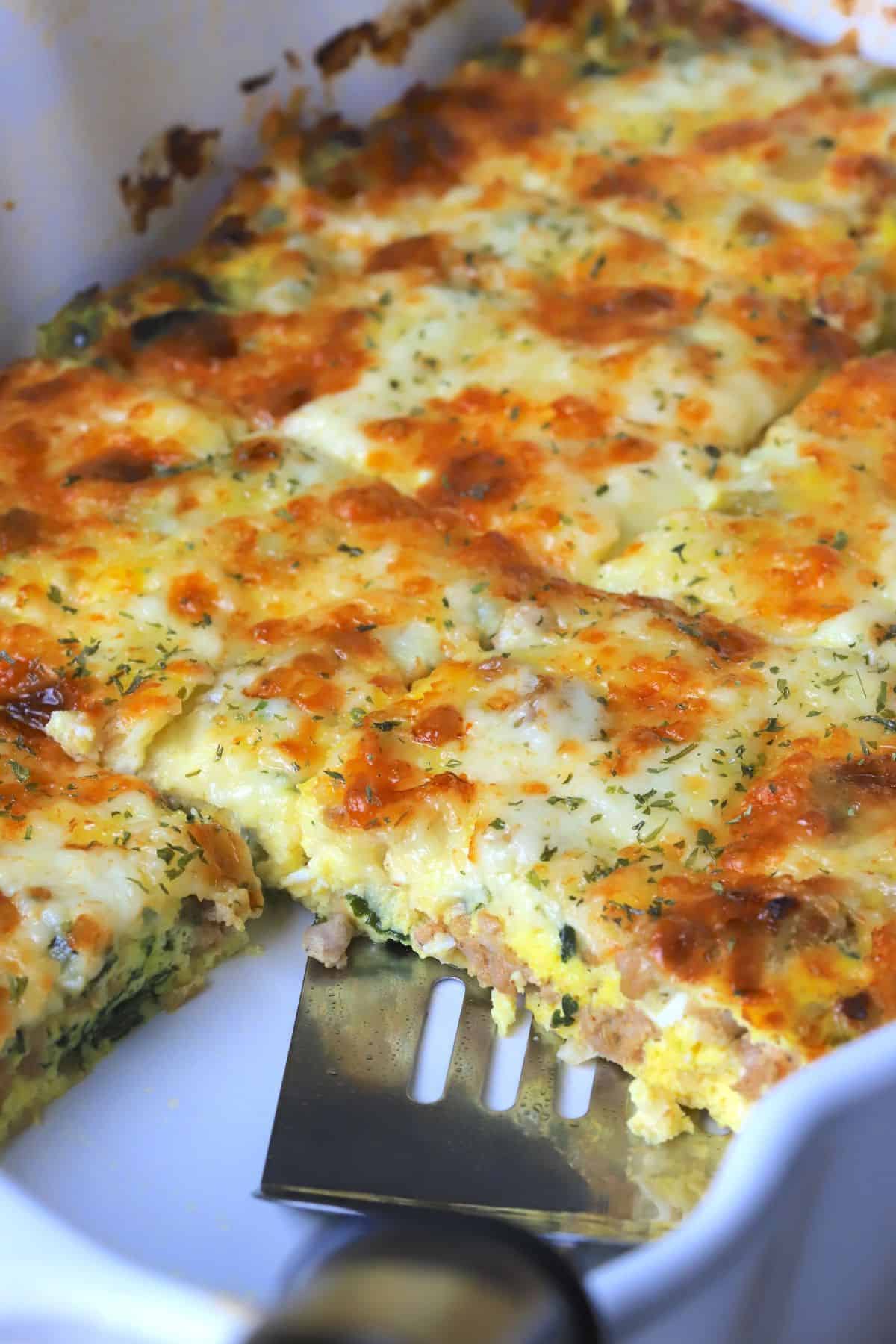 The casserole dish with the frittata in rectangle slices with a spatula.