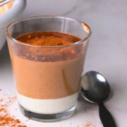 A glass with greek yogurt in the bottom then filled with the low carb tiramisu chia pudding sprinkled with cocoa powder.