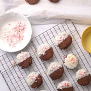 Low carb white chocolate dipped peppermint cookies on a wire rack next to bowl with crushed peppermint candy.