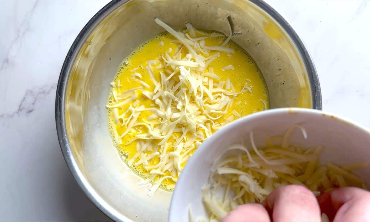 Adding shredded cheese to the egg mixture in a bowl.