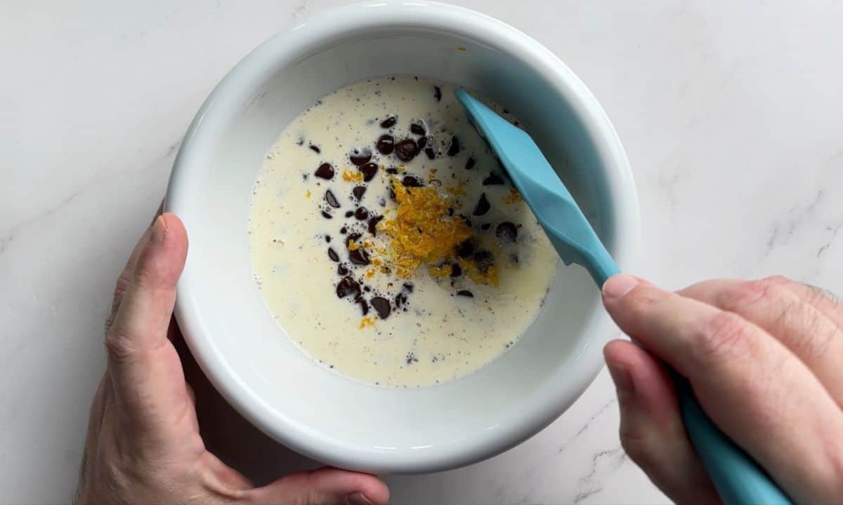 Overhead shot of a white bowl with cream, chocolate chips and orange zest.