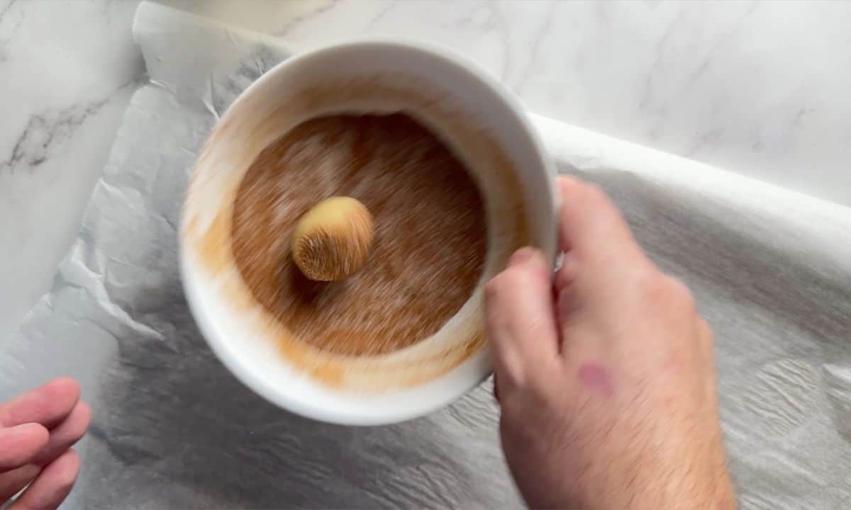 Rolling the cookie dough ball in the cinnamon sweetener mixture.