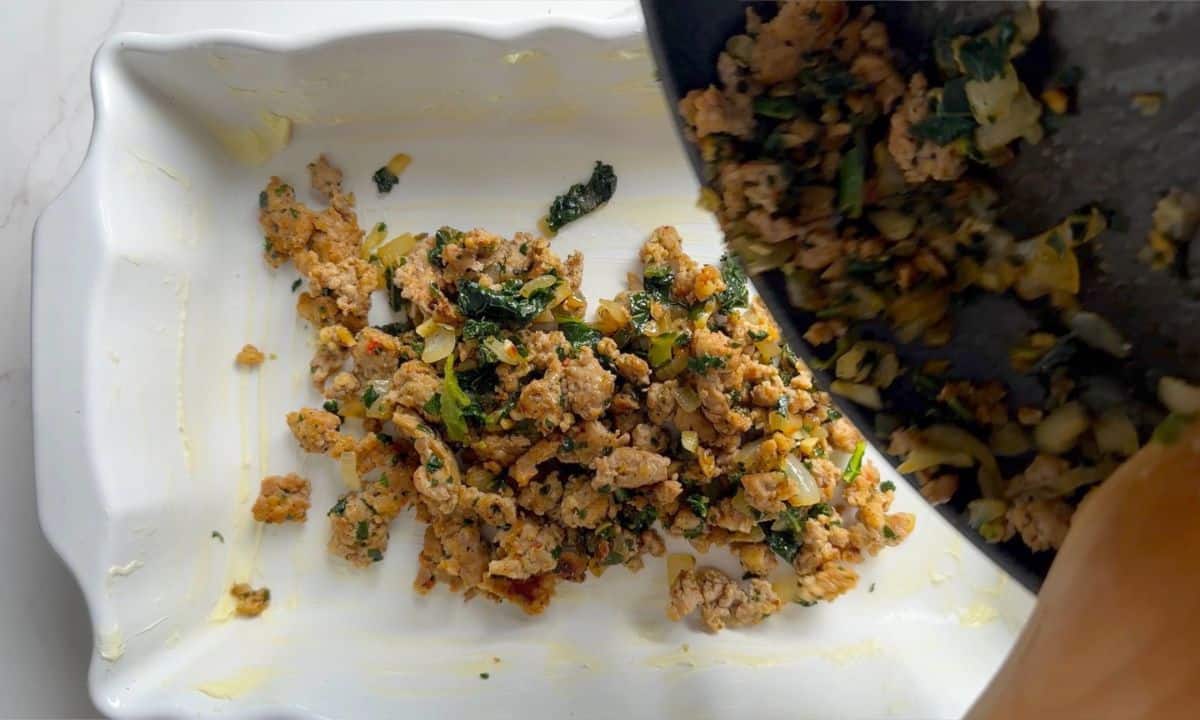 Transferring the sausage and kale mixture into the casserole dish.