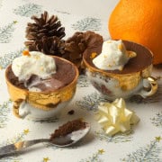 Orange chocolate pots in teacups next to acorns, and orange and a spoon.