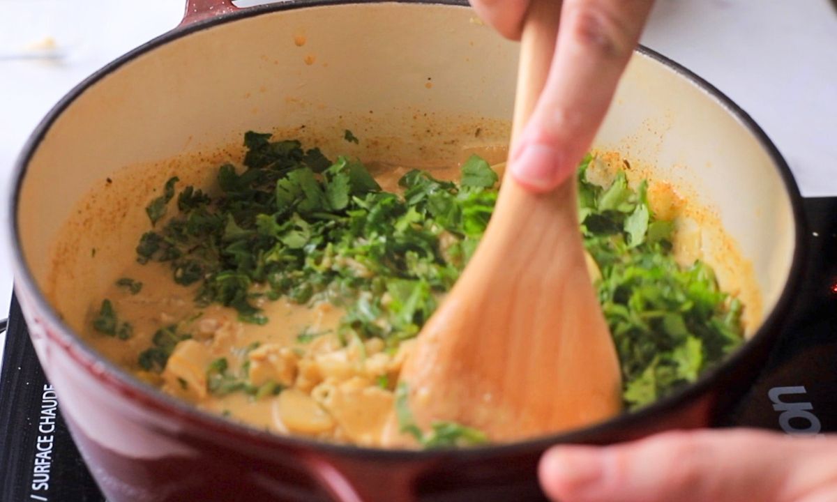 Large pot of chicken chili with cilantro and a wooden spoon stirring.