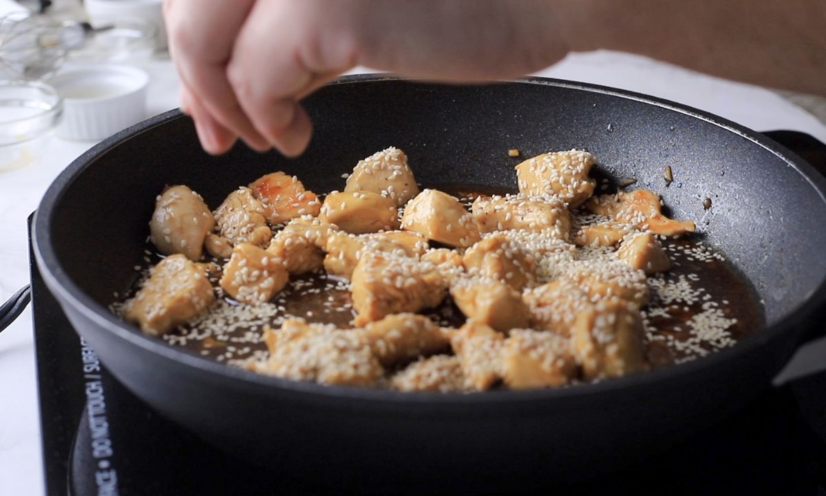 Sprinkling sesame over the cooked chicken in the skillet.