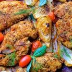 Baked italian chicken with fennel, tomatoes and oinons on a parchment lined baking sheet.