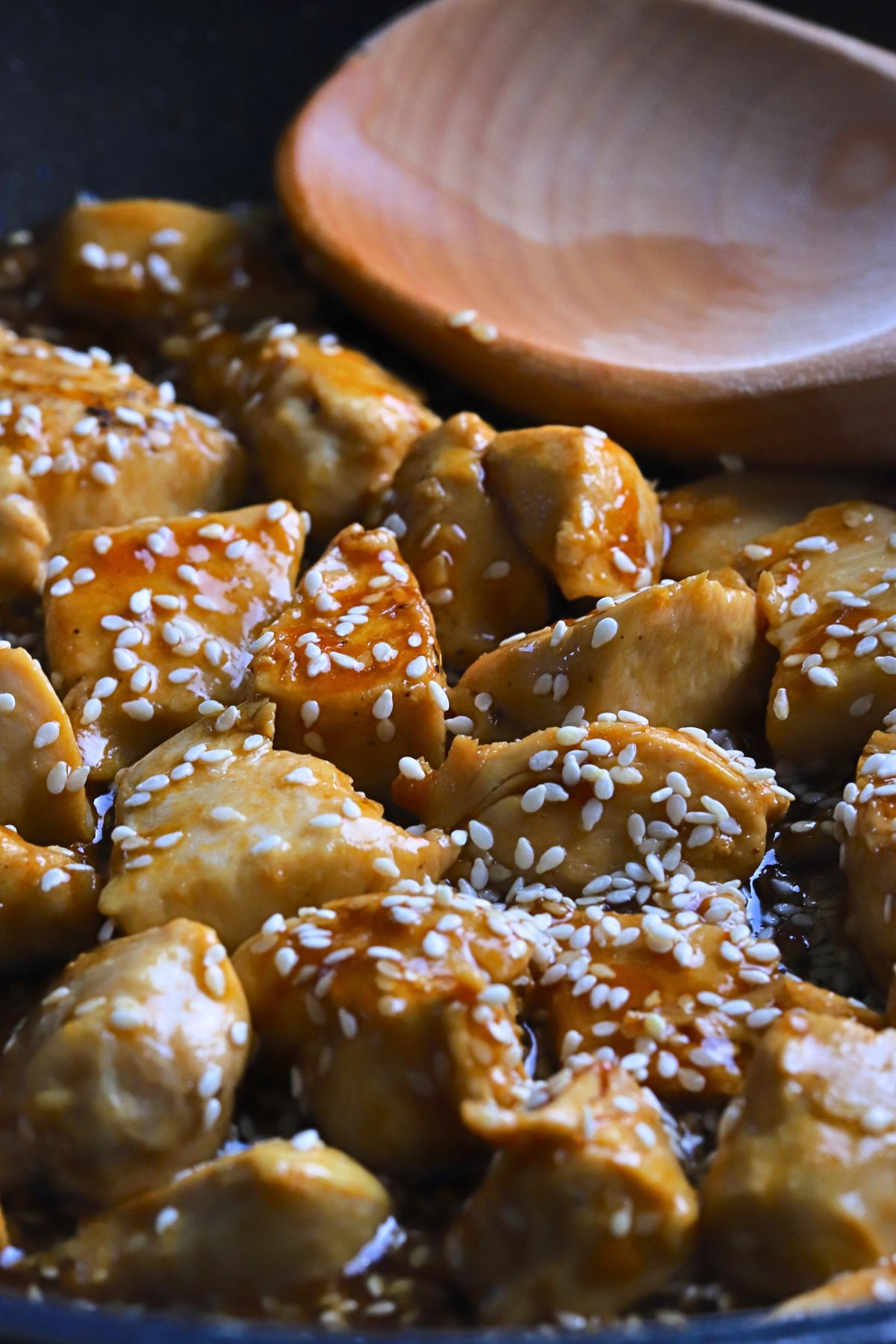 Closeup of the low carb sesame chicken in the skillet with a wooden spoon.