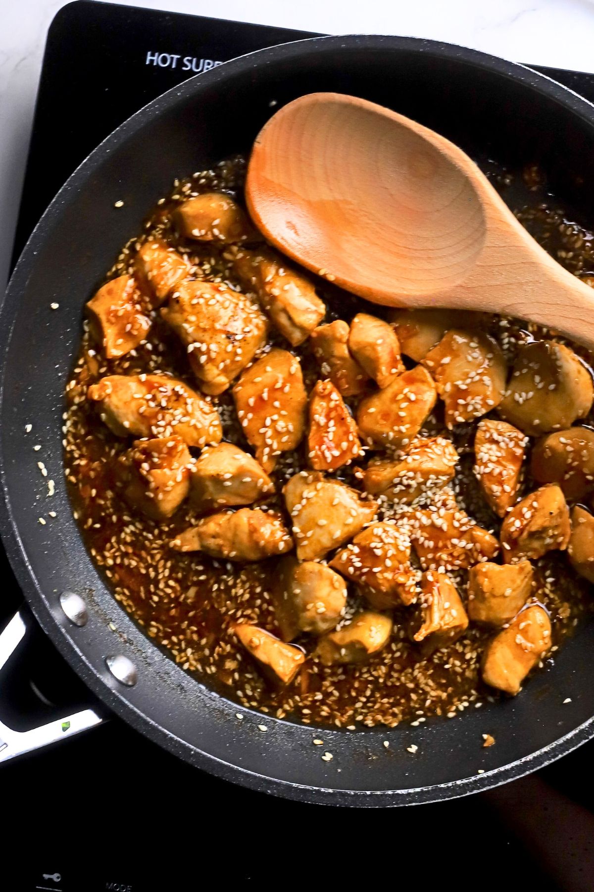 Low carb sesame chicken in a skillet with a wooden spoon.