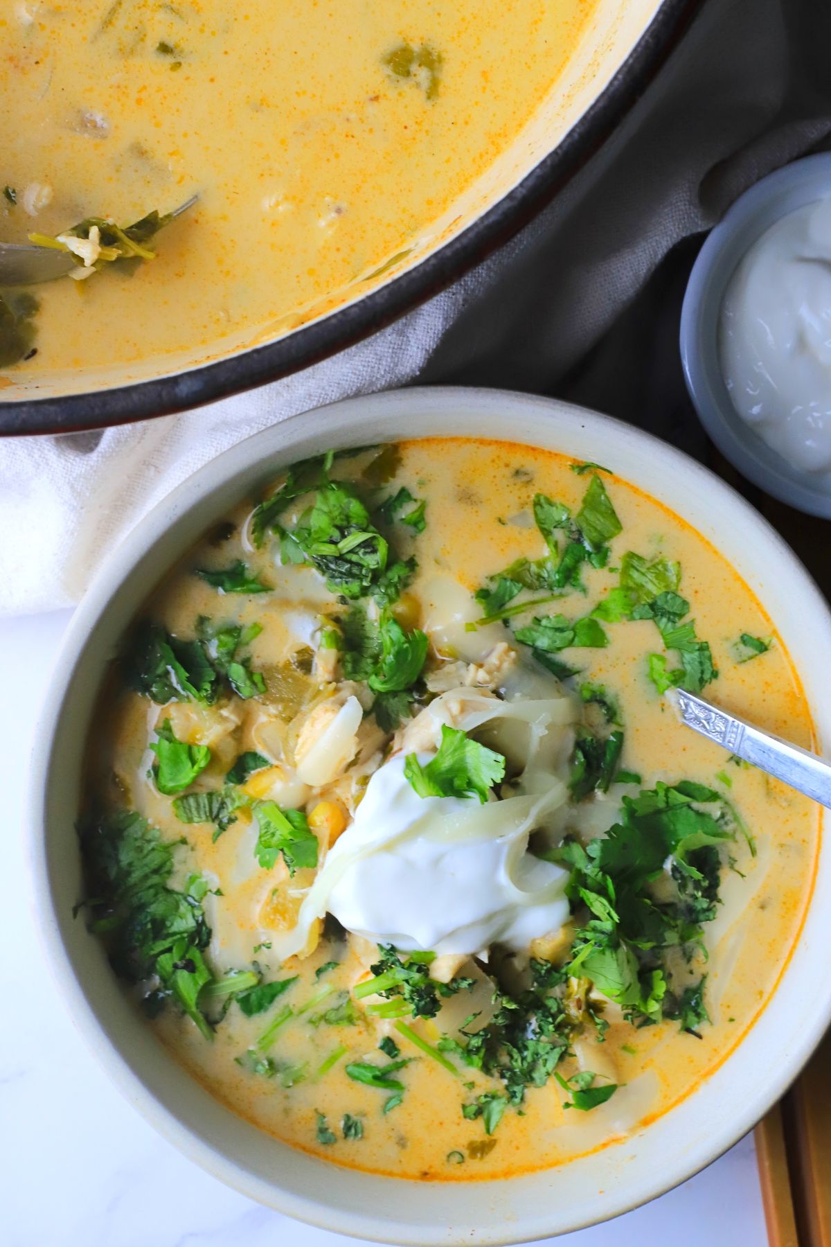 Low carb white chicken chili in a bowl topped with cilantro and sour cream next to a pot of the same.