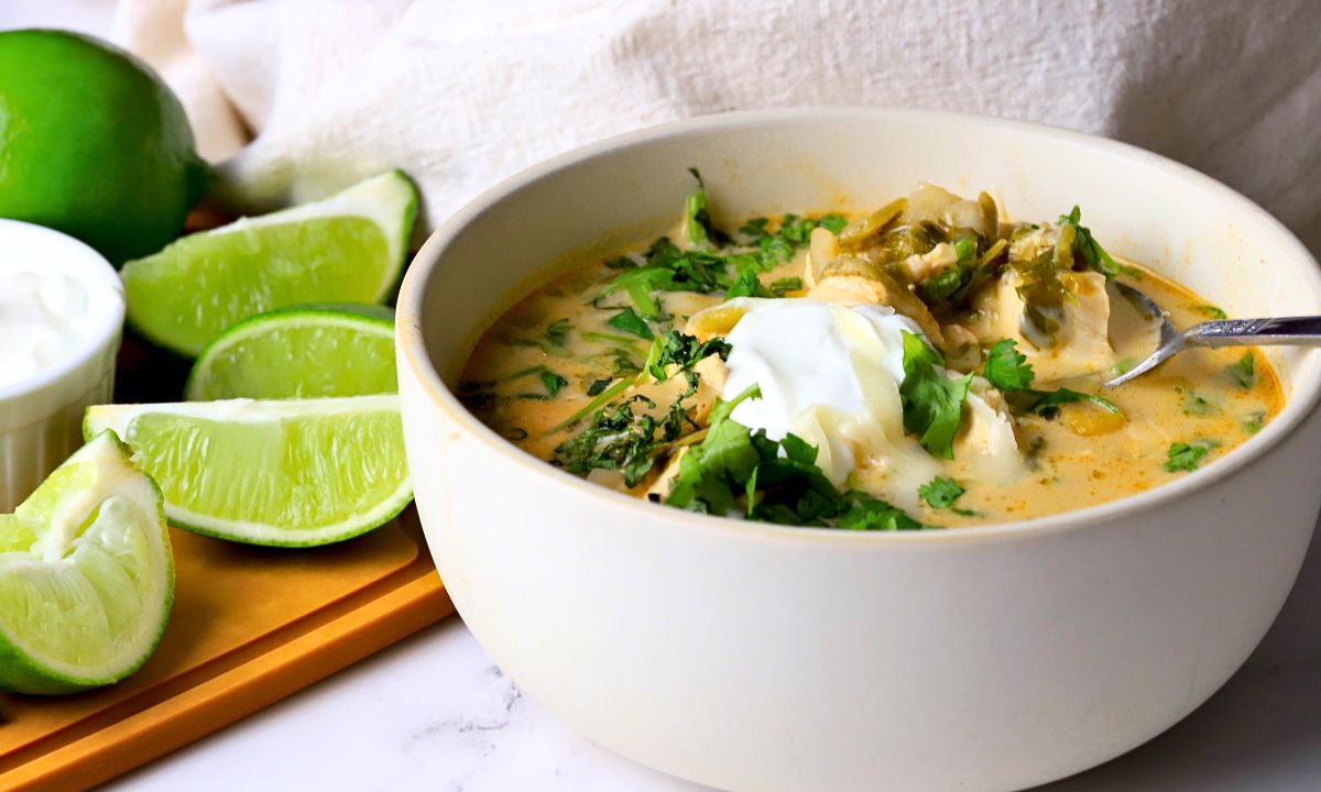 Low carb white chicken chili in a bowl topped with cilantro and sour cream next to some limes.