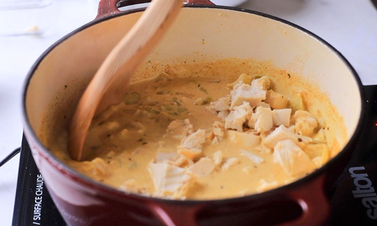 Large pot on the stove with chicken chili and a wooden spoon.