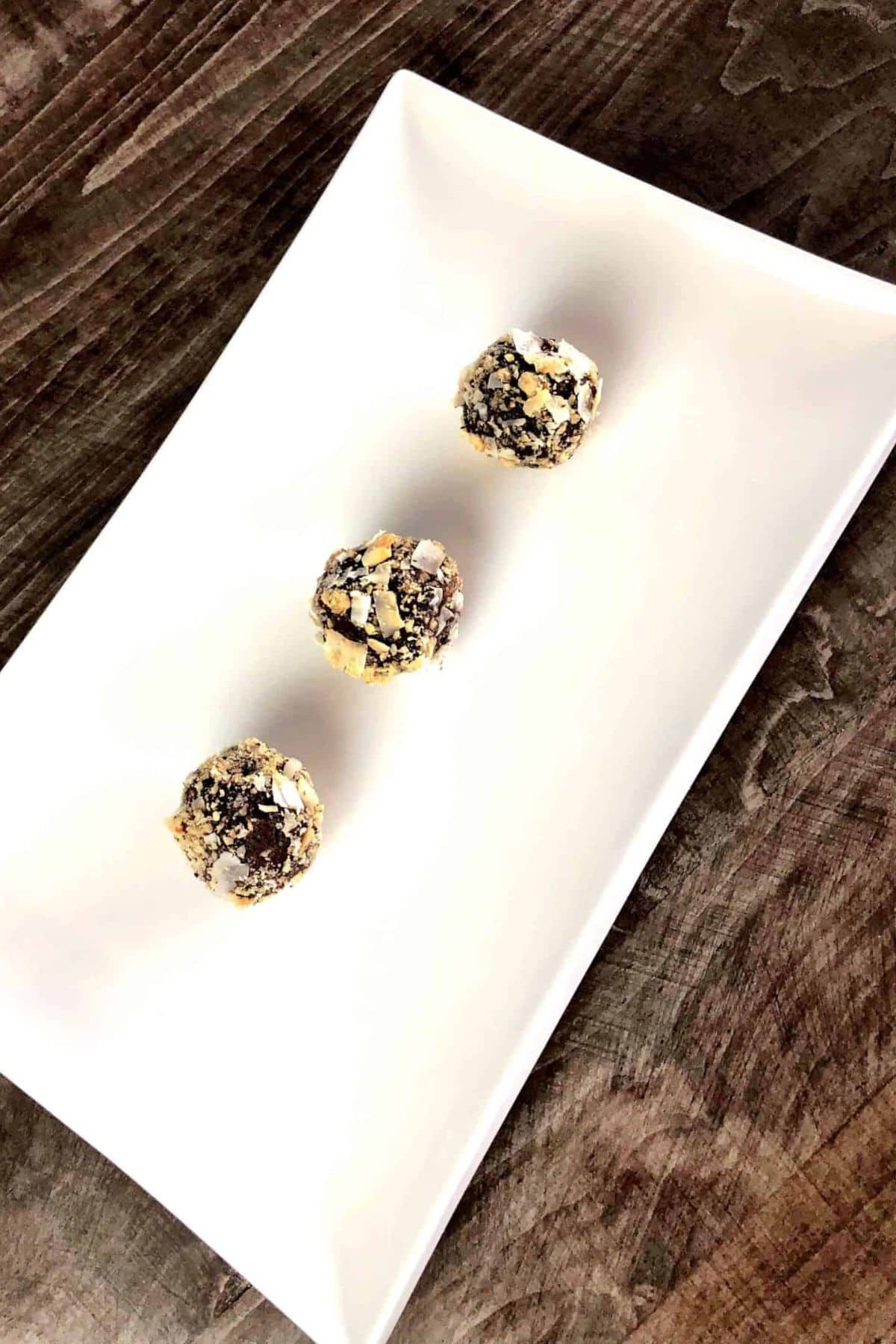 Three chocolate coconut nut balls on a white plate.