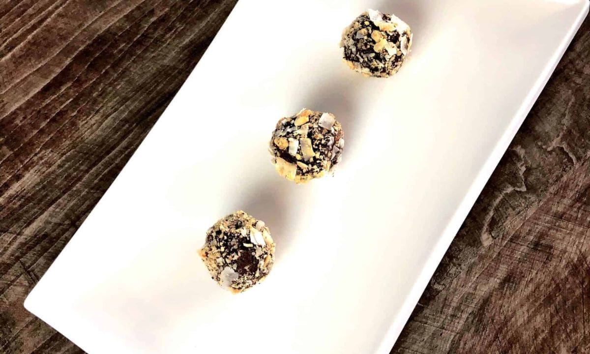 Three chocolate coconut nut balls on a white plate.