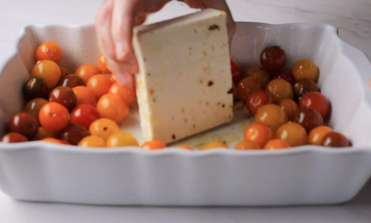 Adding the block of feta to the tomatoes in the casserole.