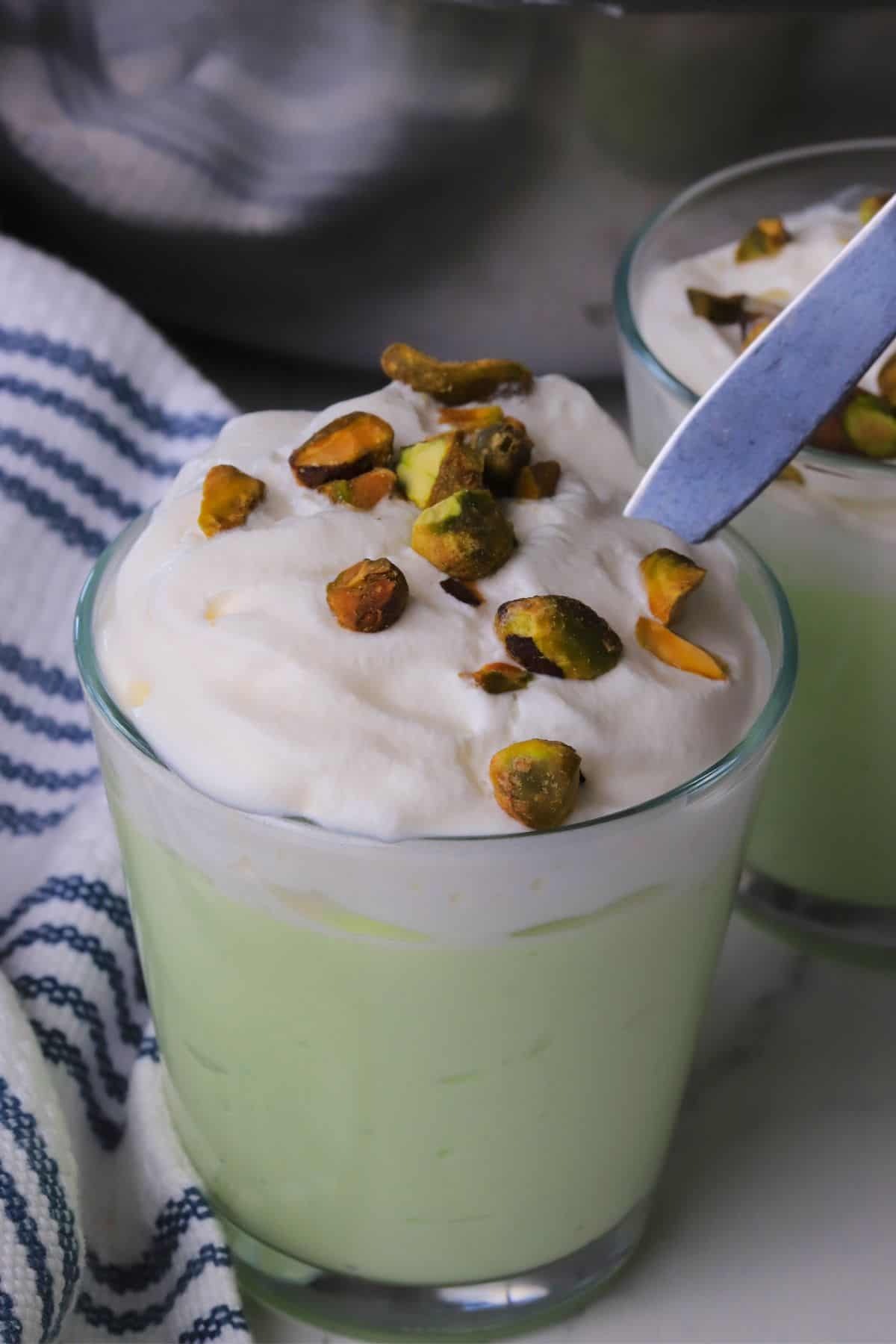 High protein pistachio pudding in a glass cup topped with whipped cream and crushed pistachios.