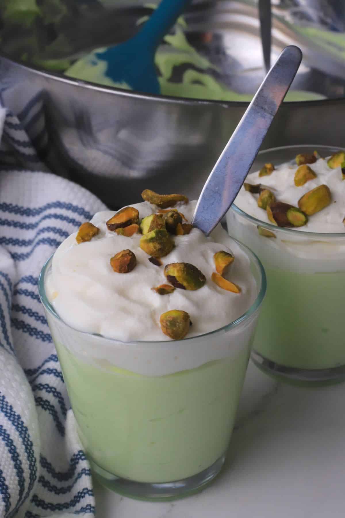 High protein pistachio pudding in a glass cup topped with whipped cream and crushed pistachios.