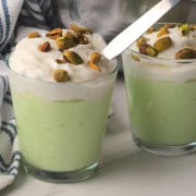 High protein pistachio pudding in a glass cup topped with whipped cream and crushed pistachios.