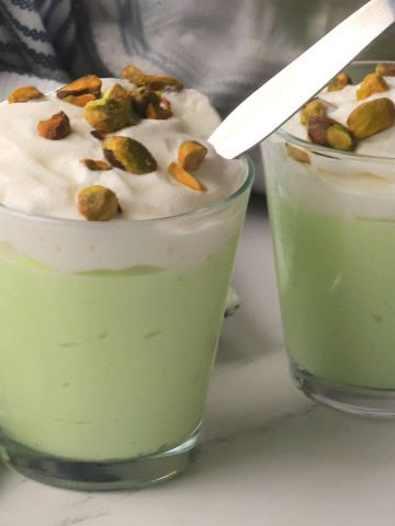 High protein pistachio pudding in a glass cup topped with whipped cream and crushed pistachios.
