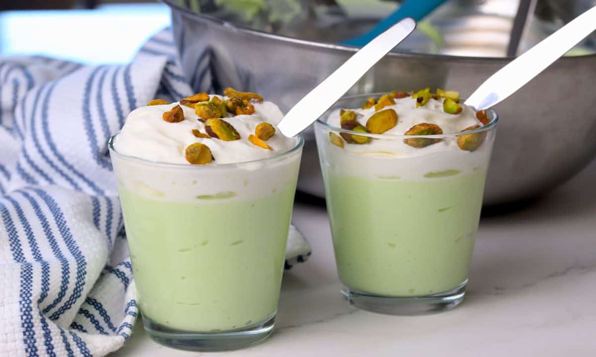 High protein pistachio pudding in a glass cup topped with whipped cream and crushed pistachios.