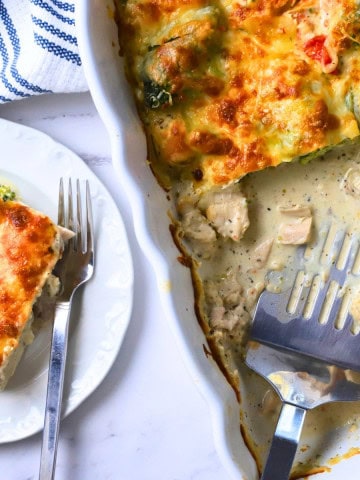 A slice of low carb italian chicken veggie casserole on a plate with the casserole dish next to it.