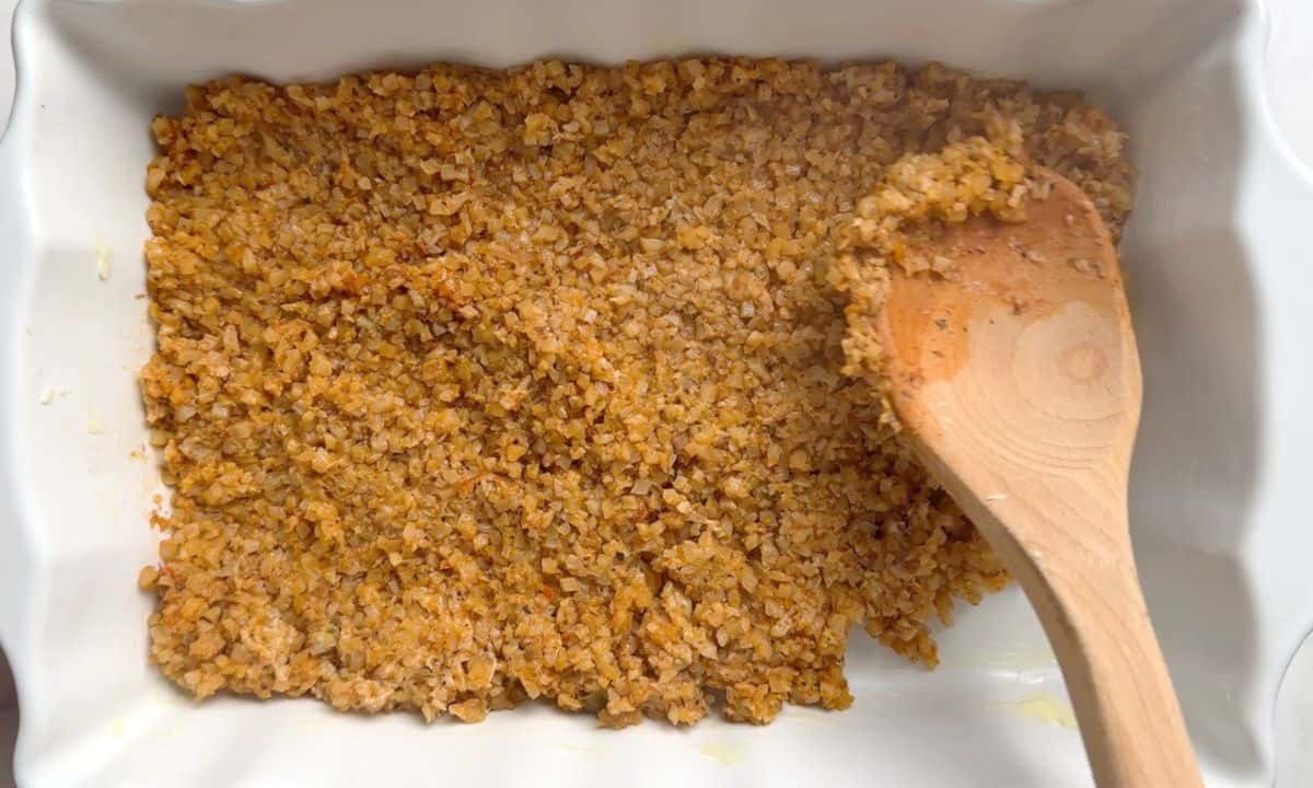 Spreading the cauliflower rice in the casserole dish with a wooden spoon.