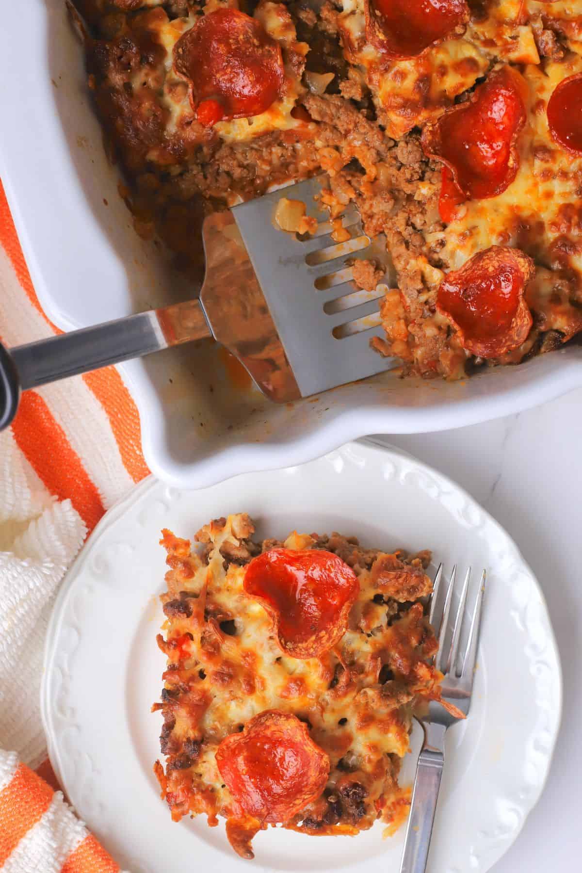 Low carb pizza casserole slice on a plate with the casserole in the background.