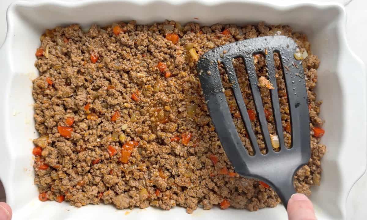 Spreading out the ground beef in the casserole dish.